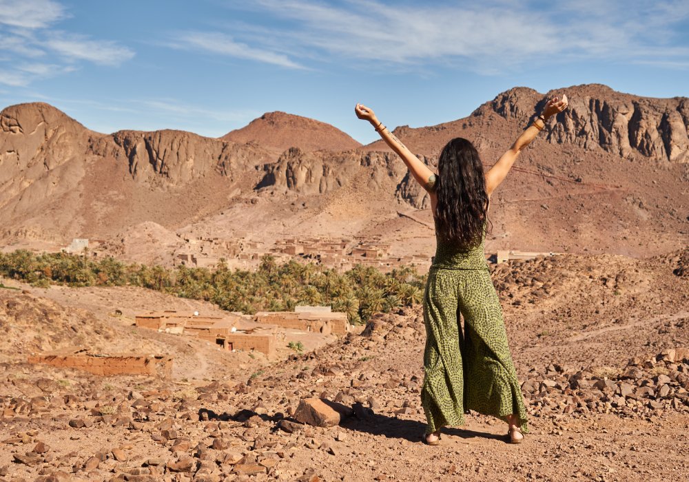 A woman in a green dress stands on a mountain in Morocco.